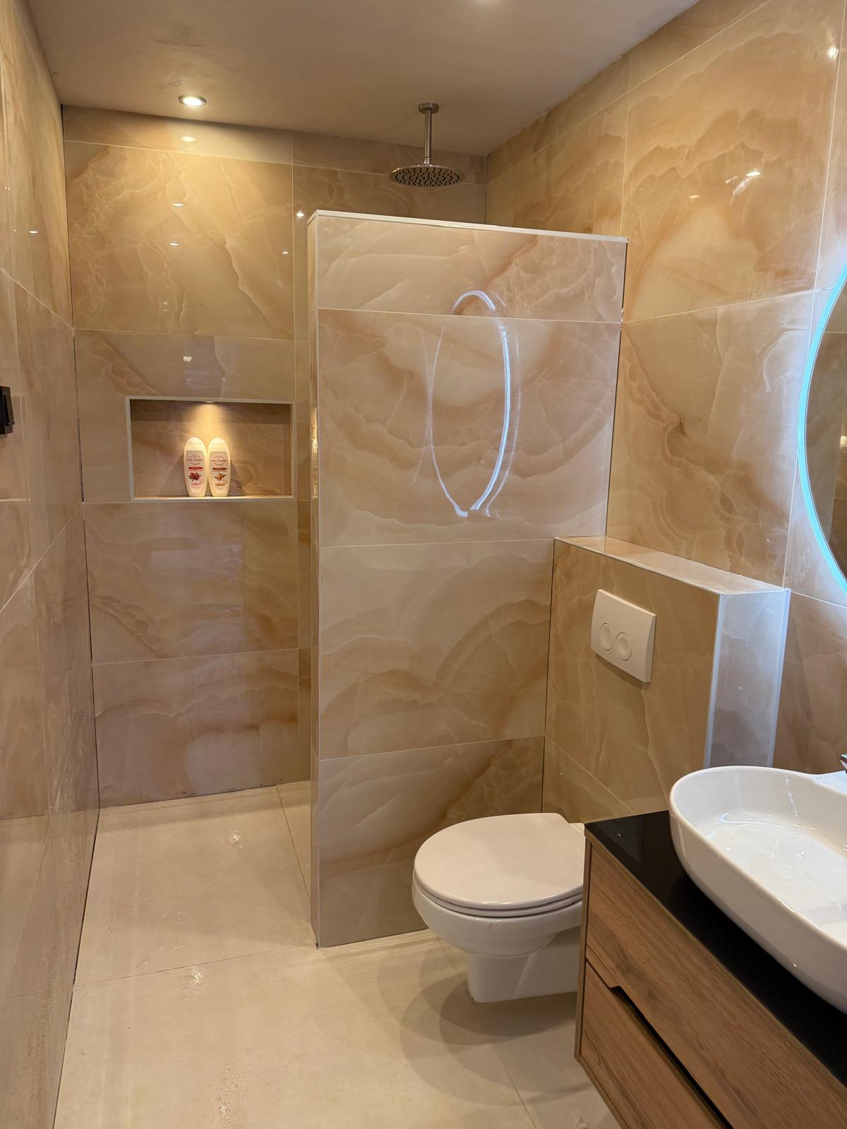 Badkamer met beige marmerlook tegels, inloopdouche met nis en hangtoilet